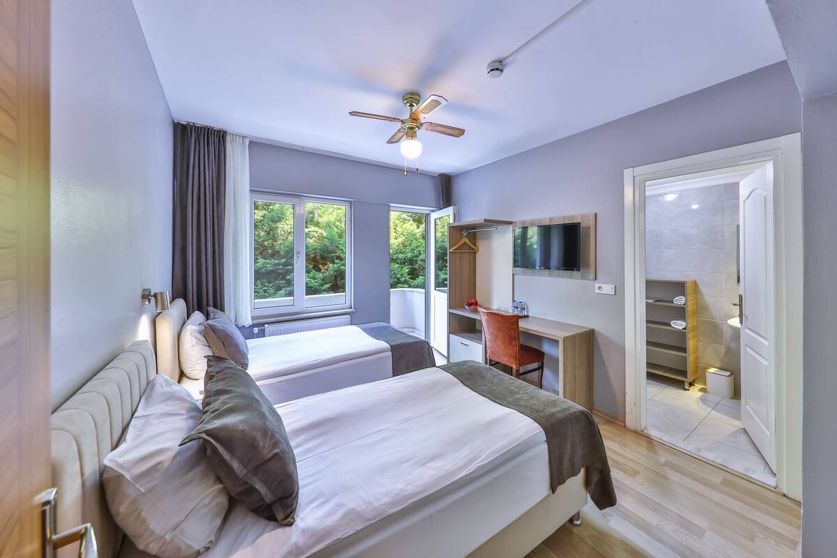 A modern bedroom with two beds, a desk, and a TV.