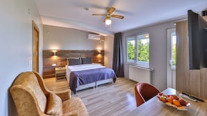 Una habitación de hotel moderna con cama, escritorio, silla, ventilador de techo y ventana con vista a zonas verdes.