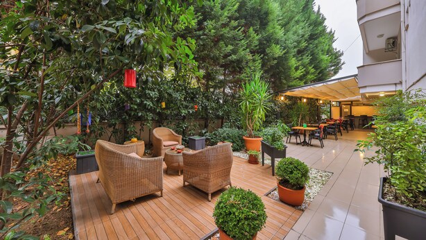 Un patio al aire libre con mobiliario de mimbre, plantas en macetas y una terraza de madera.