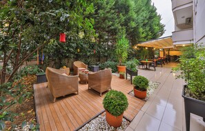An outdoor patio area with wicker furniture, potted plants, and a wooden deck. - Palmada Hotel (Adapazari)