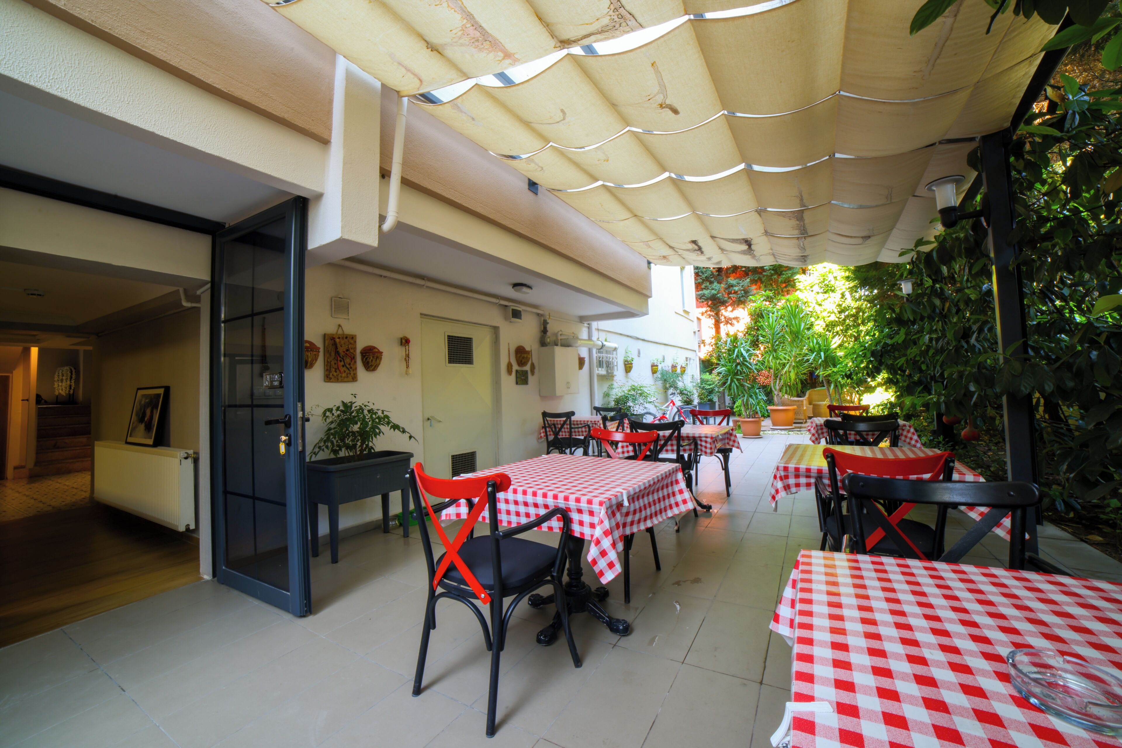 An outdoor patio area with tables and chairs, covered by a canopy, and surrounded by potted plants.