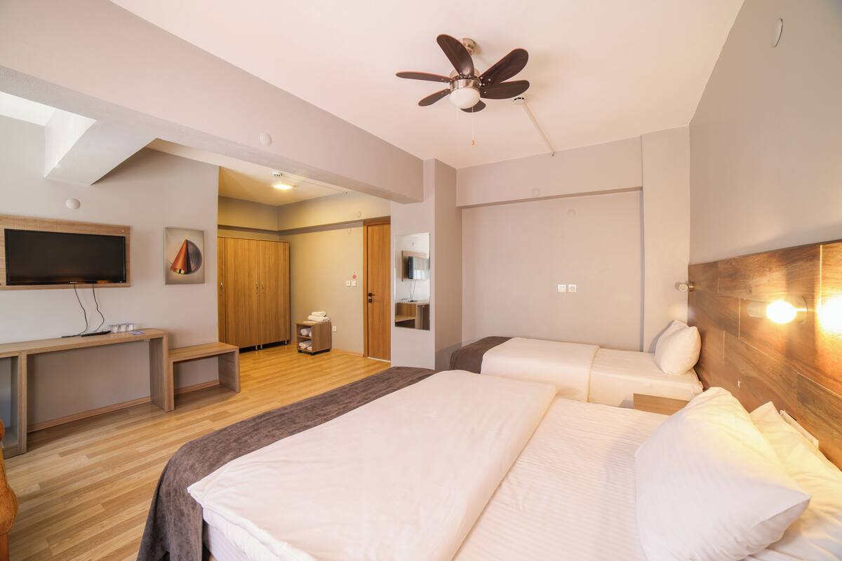 A hotel room with a bed, a desk, a TV, a ceiling fan, and a wooden headboard.