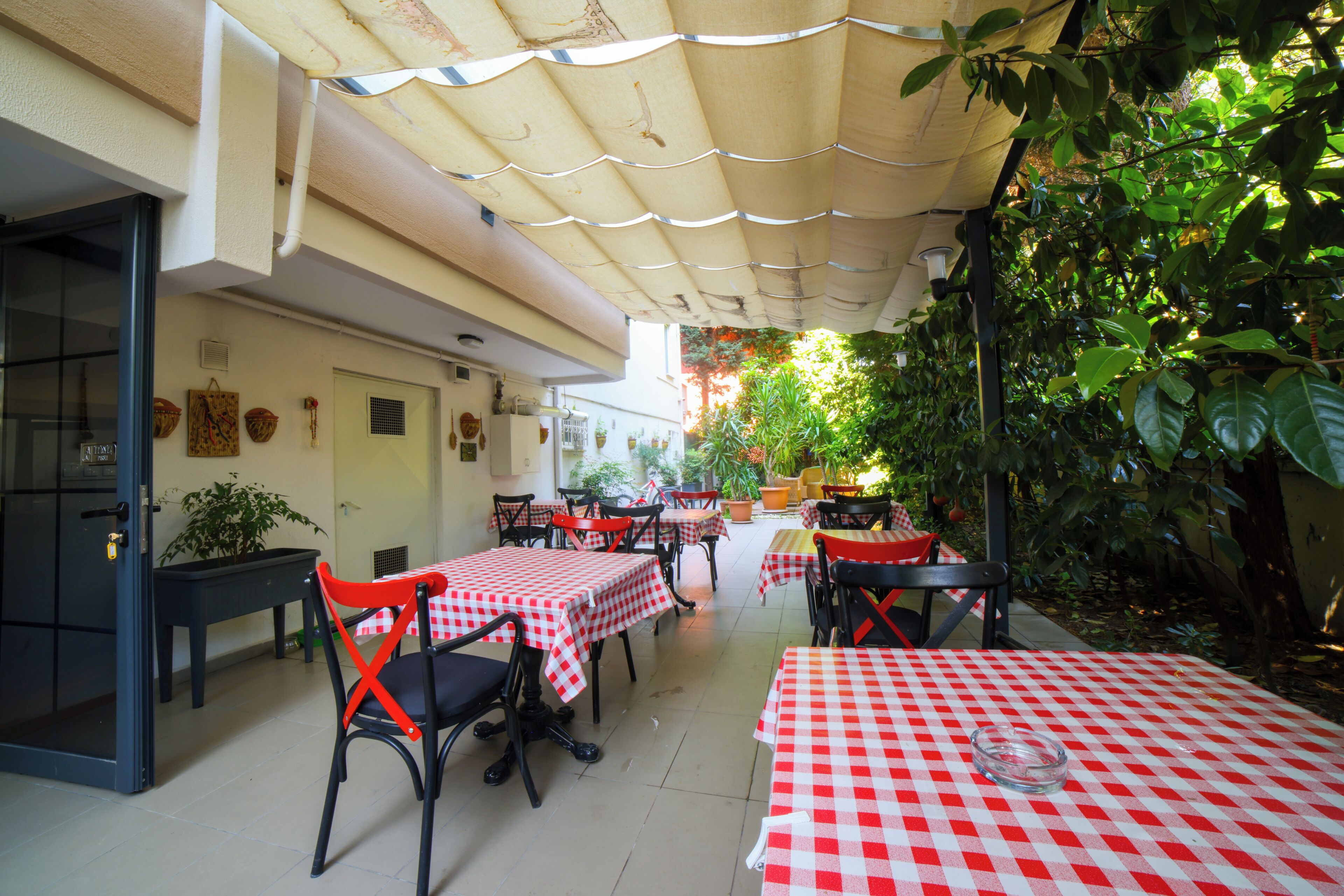 An outdoor dining area with tables and chairs, a covered walkway, and potted plants.