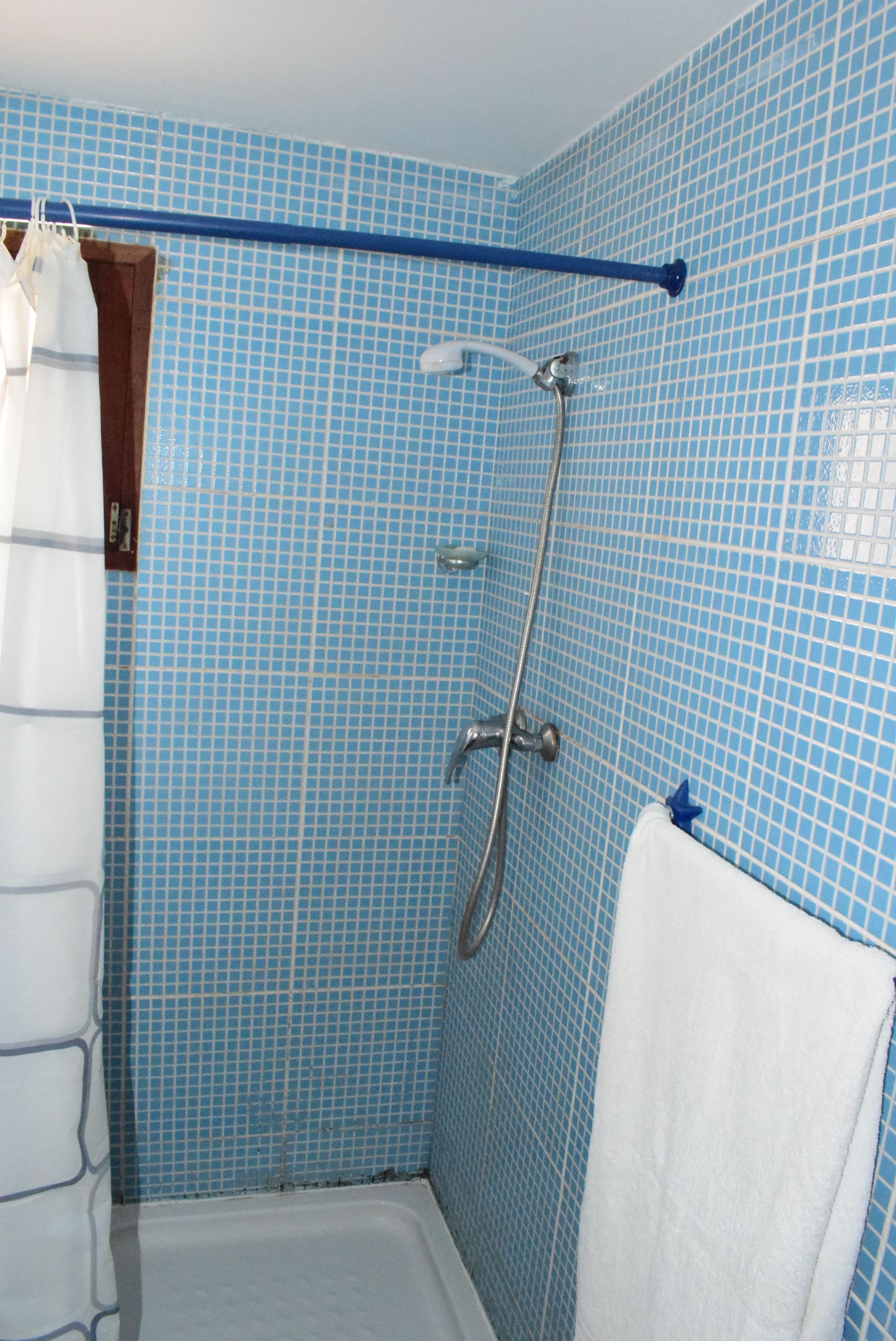 Un baño con paredes de azulejos azules, una ducha, una bañera blanca y un perchero para toallas.