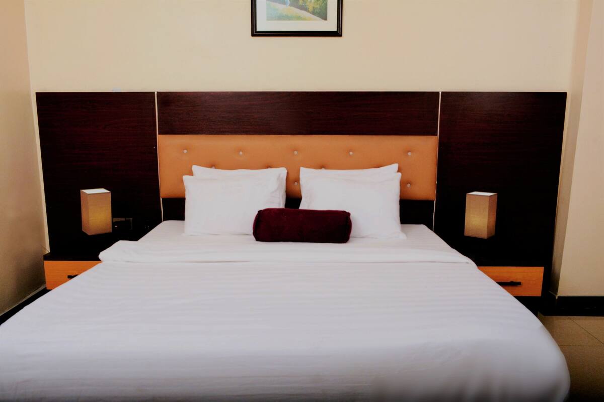 Une chambre d’hôtel avec un grand lit, deux tables de chevet, une tête de lit en bois et deux lampes fixées au mur.