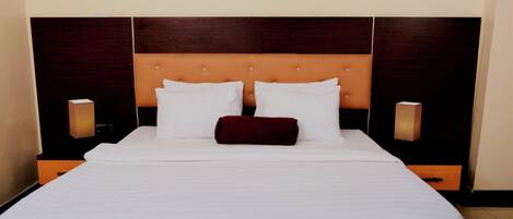 A hotel room with a large bed, two bedside tables, a wooden headboard, and two wall-mounted lamps.