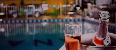 A glass of red wine and a bottle in a metal bucket by a pool.
