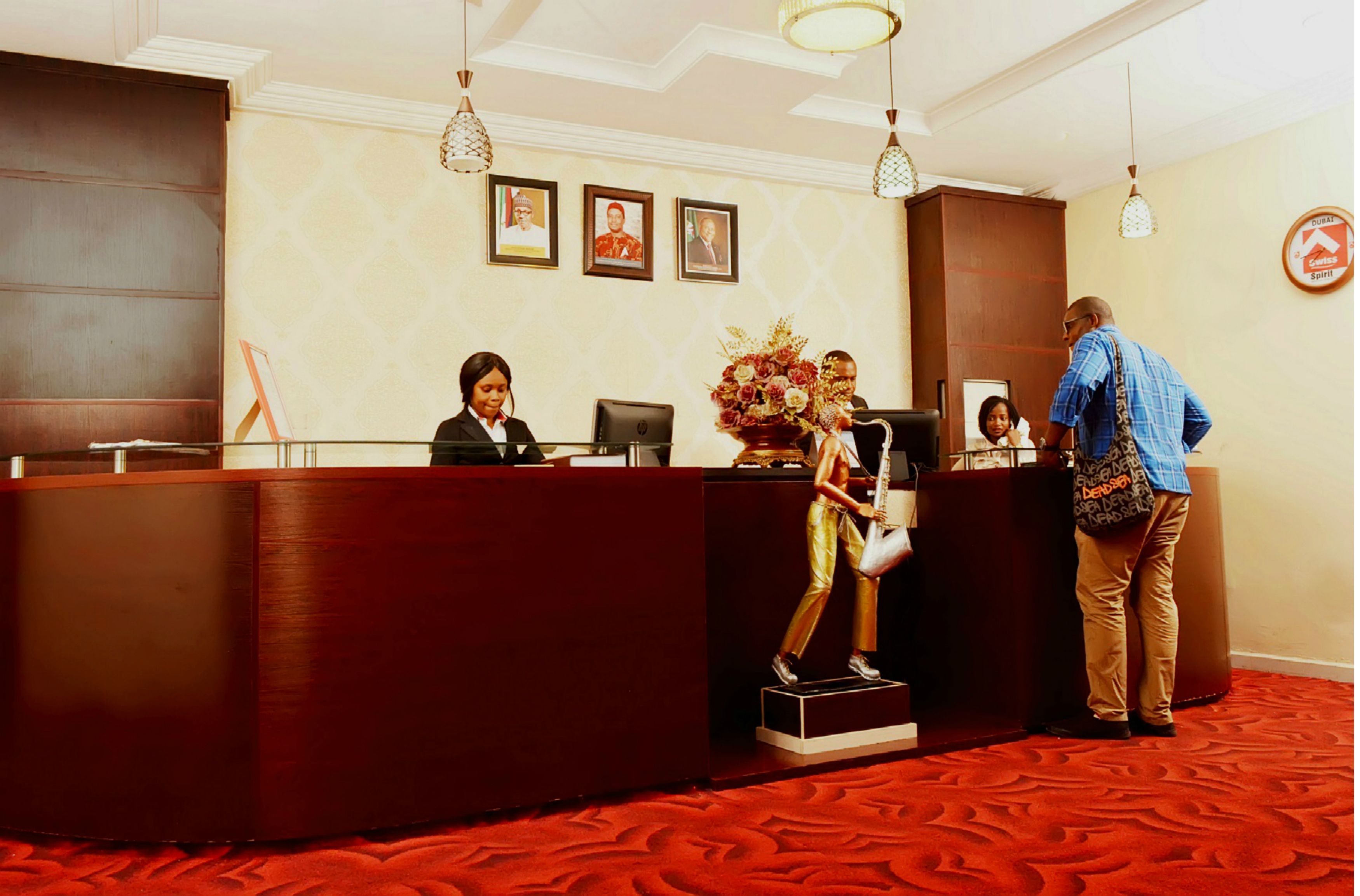 A reception desk with a receptionist, a statue, and a man standing.