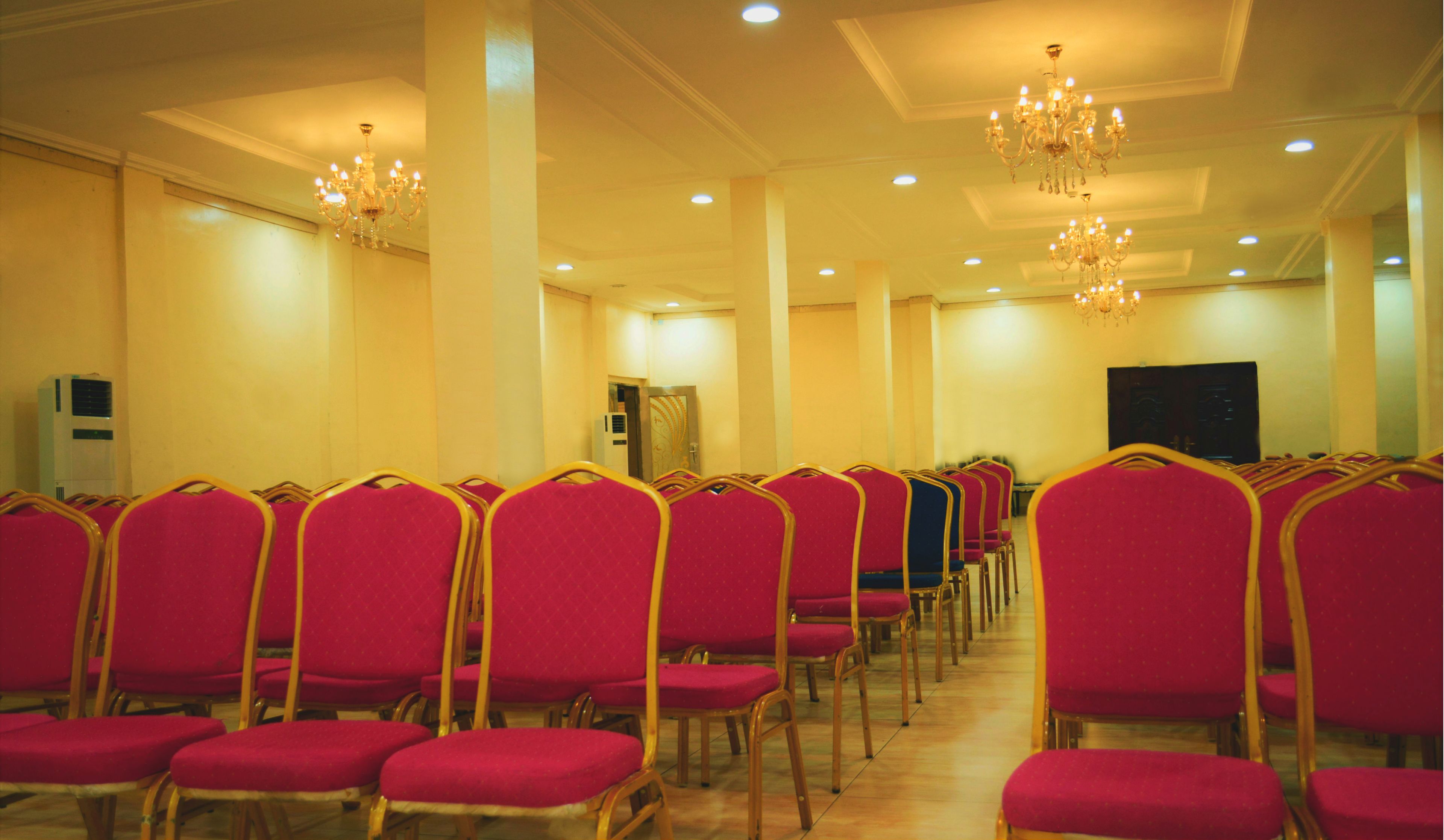 Rows of red chairs with gold frames in a room with cream walls and a chandelier.