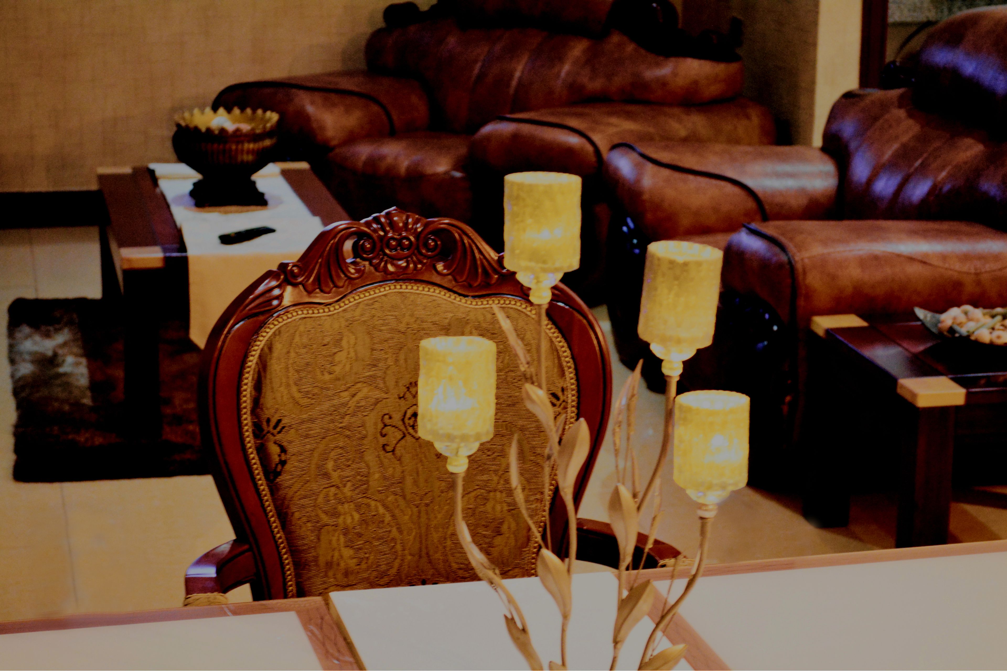 A room with a wooden chair, a table, and a brown leather sofa.