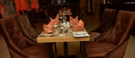 A dining area with a long table set for four, surrounded by upholstered chairs.
