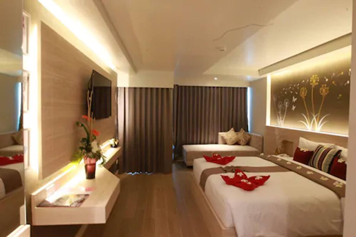 Une chambre d’hôtel avec un grand lit, un lit plus petit, un bureau avec une télévision et une œuvre d’art accrochée au mur.