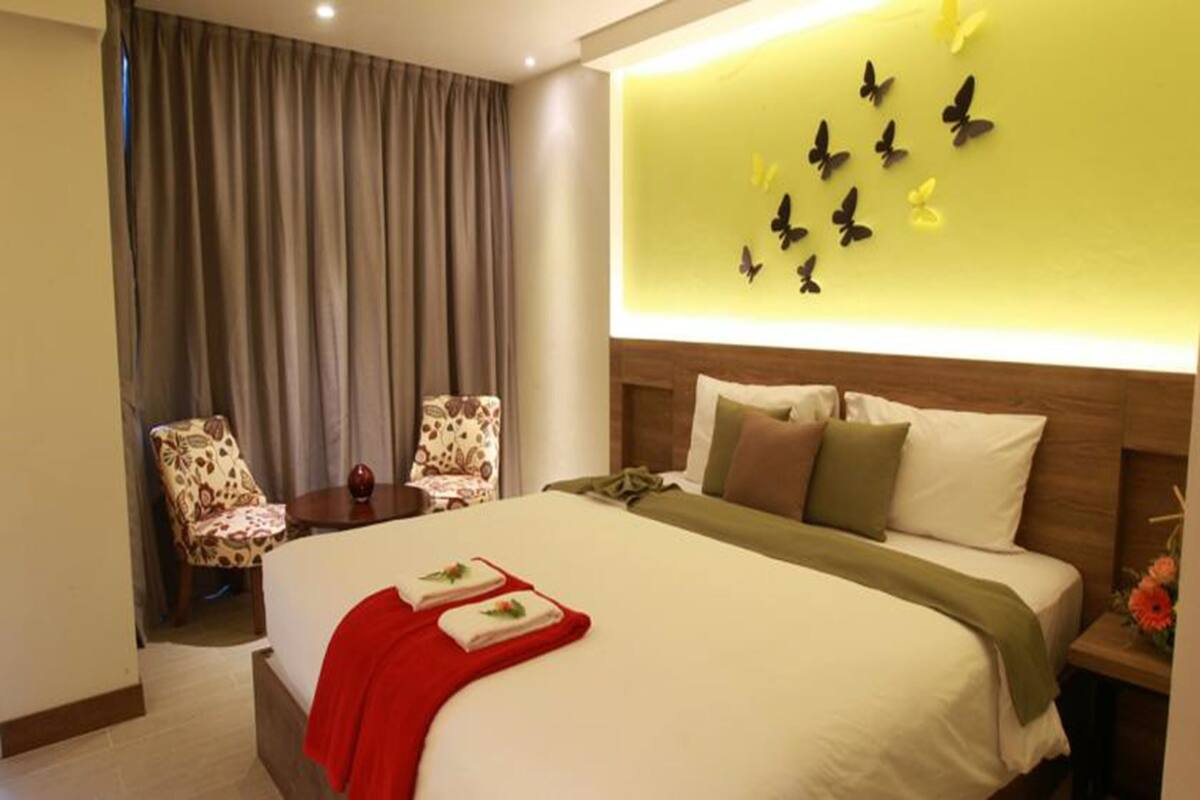Une chambre d’hôtel avec un lit, une table de chevet, une chaise et un mur décoré d’autocollants représentant des papillons.