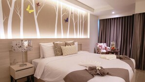 A modern hotel room with a large bed, a bedside table with a lamp, a decorative wall panel, and a view of the outside through curtains. - Levana Pattaya Hotel (Pattaya)