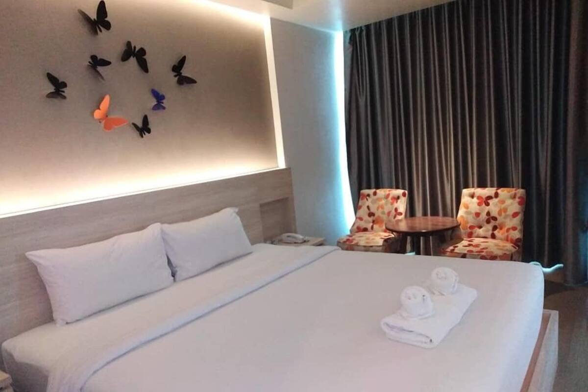 Une chambre d’hôtel avec un grand lit, deux fauteuils à motifs floraux, une petite table ronde et un téléphone fixé au mur.