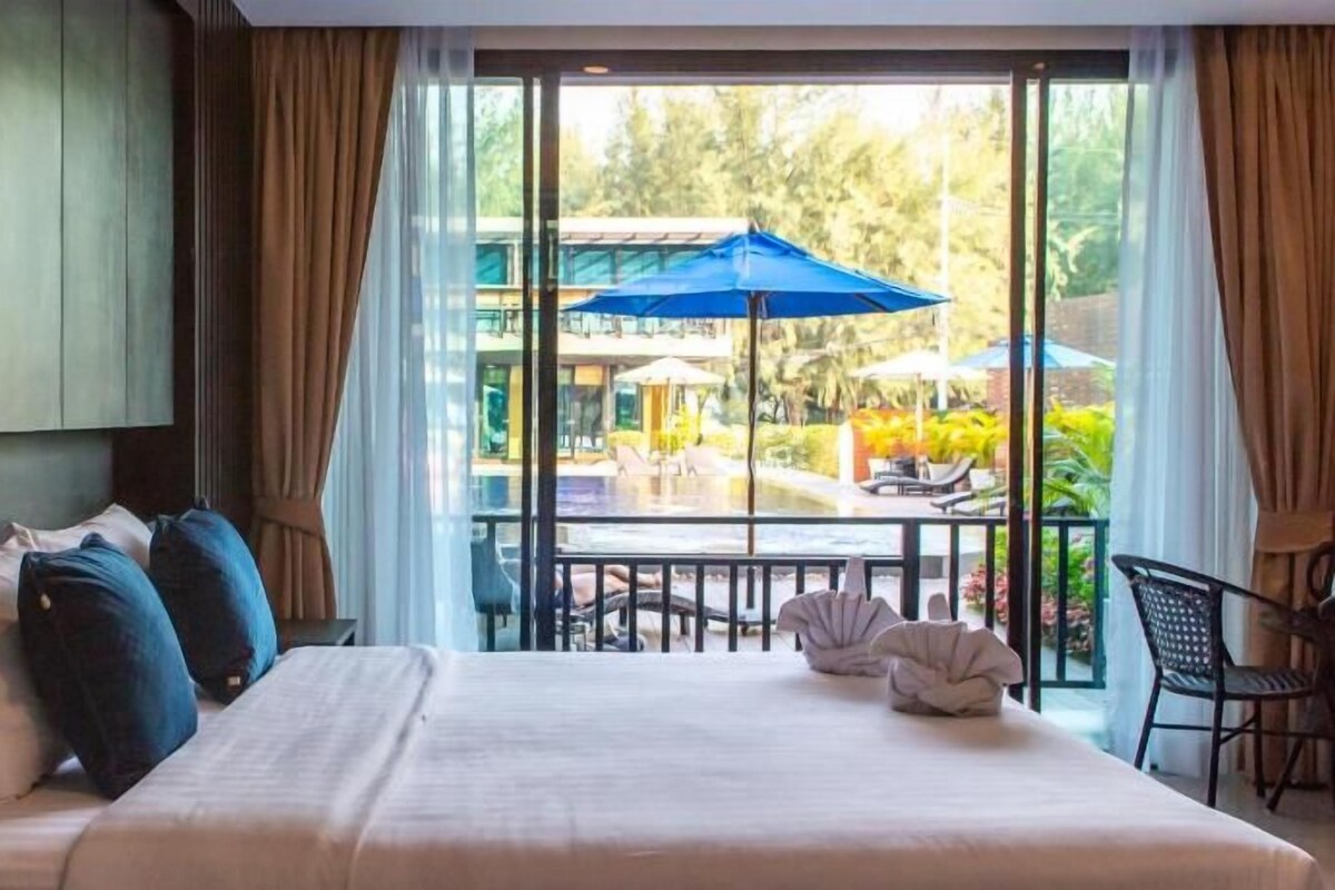A hotel room with a bed, a view of the outdoor area, and a balcony with a table and chairs.