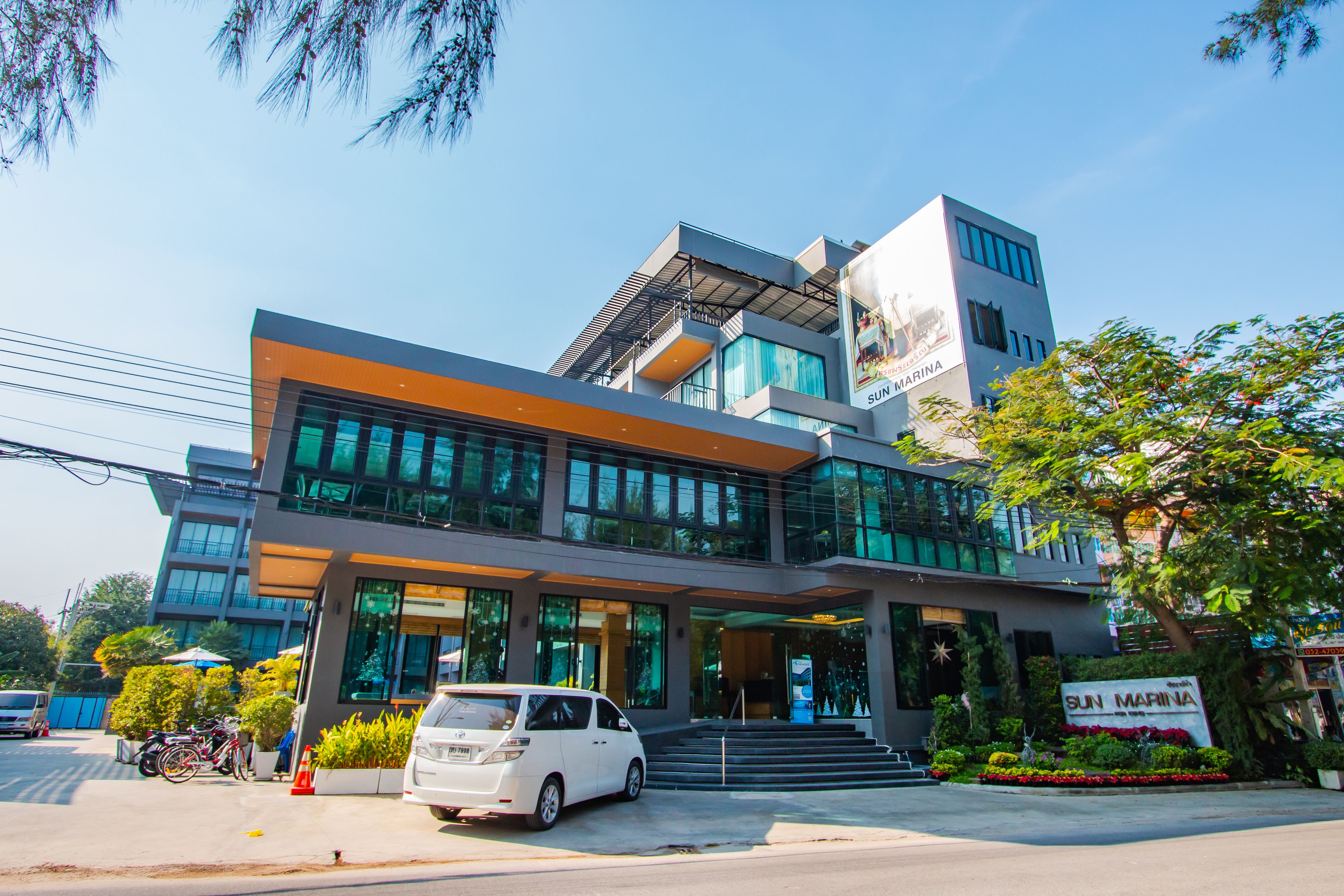 A modern building with a large glass facade, a white car parked in front, and a sign that reads "SUN MARINA".