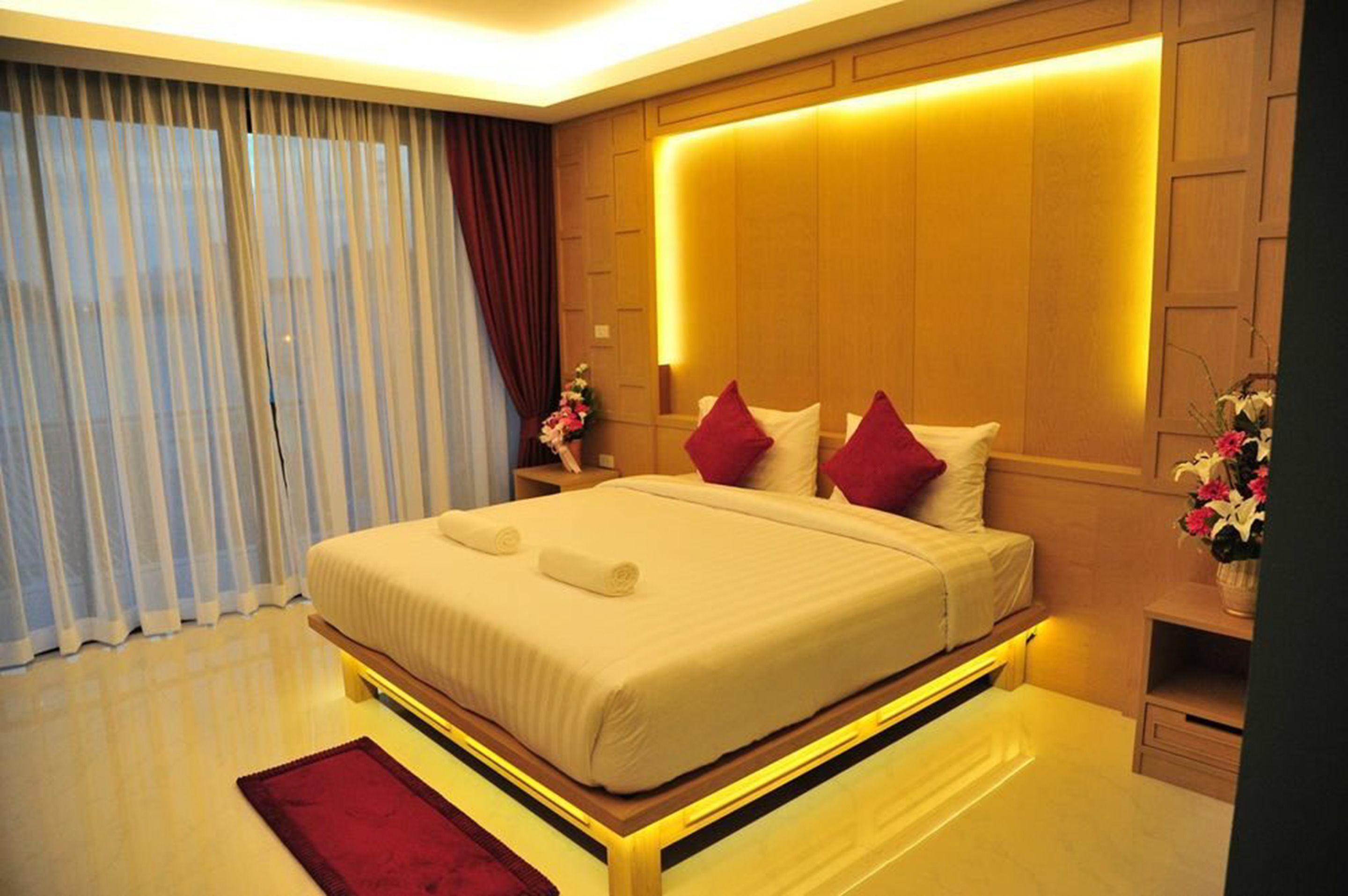 A modern hotel room with a large bed, wooden headboard, and a nightstand with a vase of flowers.