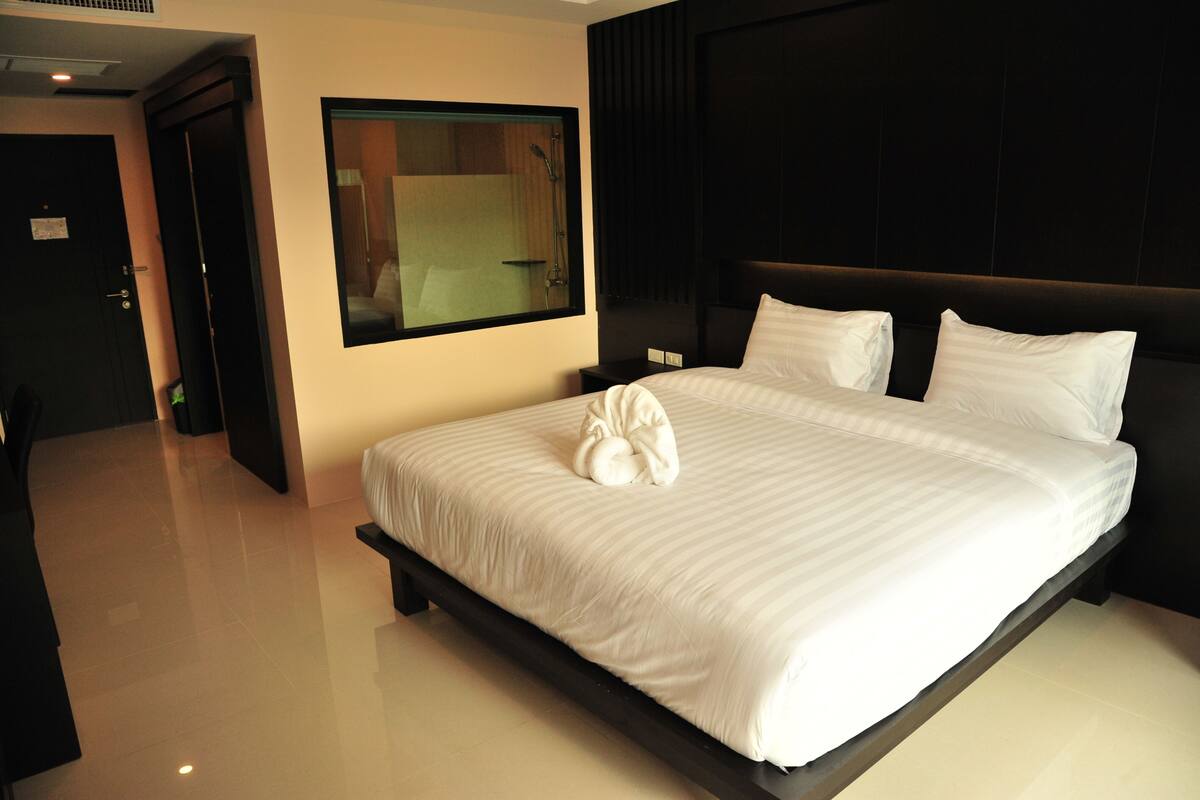 Ein modernes Hotelzimmer mit einem großen Bett, einem dunklen Kopfteil und einem großen Spiegel.