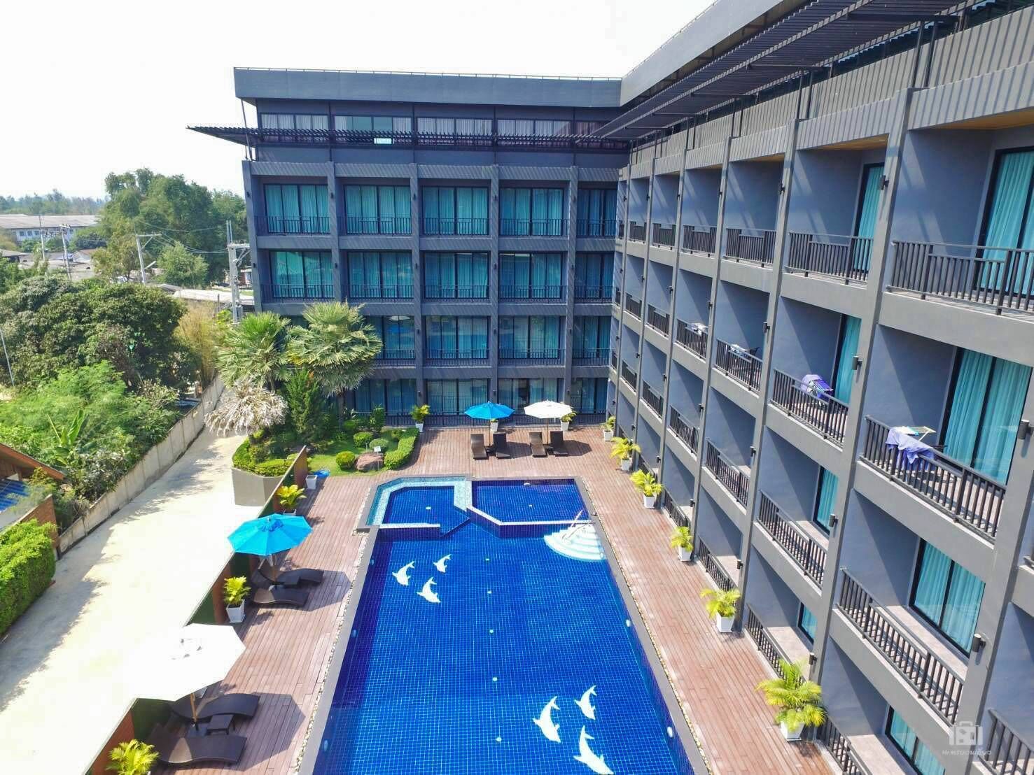 A hotel with a rooftop pool featuring dolphin designs, surrounded by lush greenery and multiple balconies.