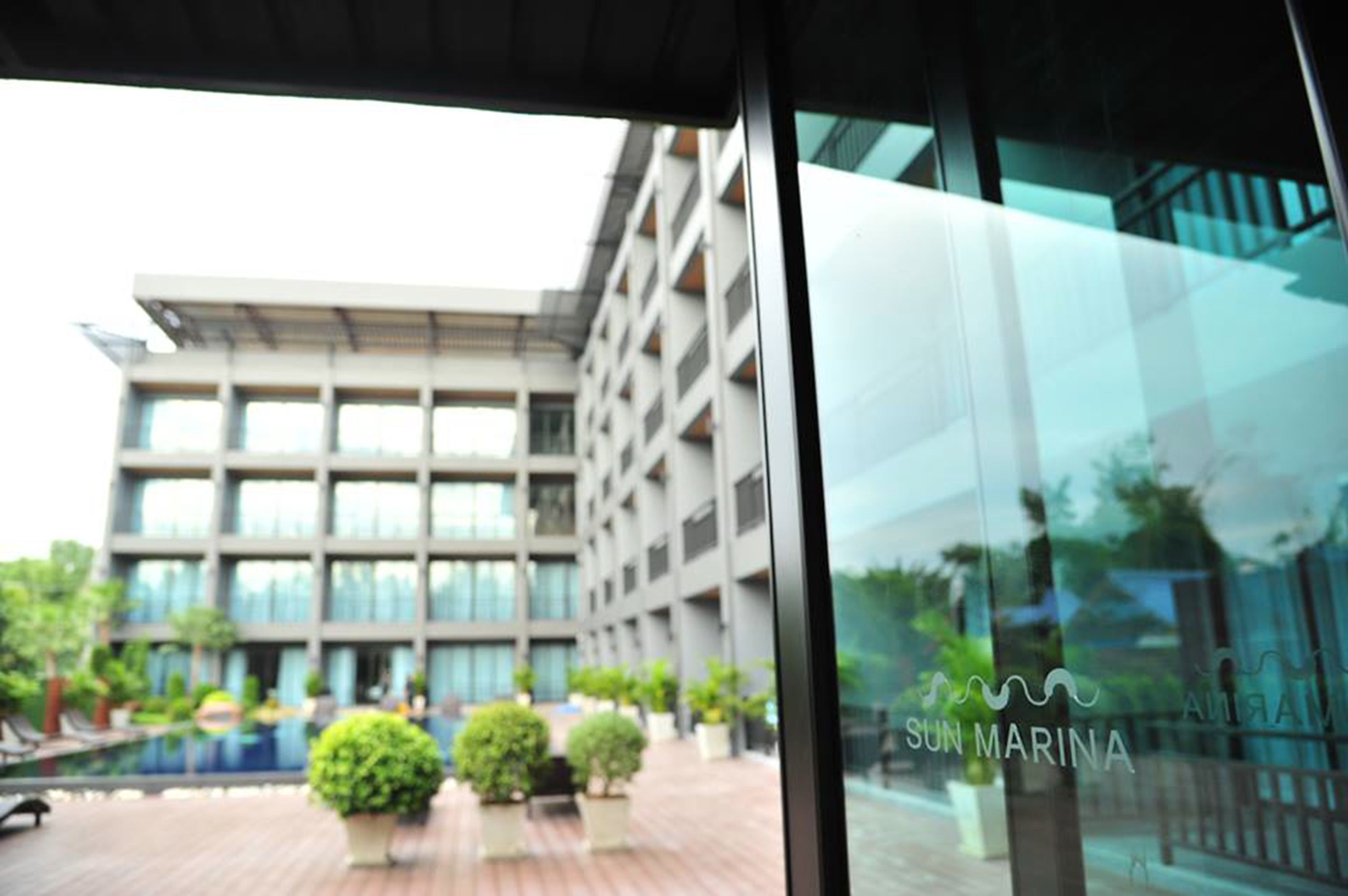 A modern building with a glass facade, a pool area with potted plants, and the text "SUN MARINA" visible.