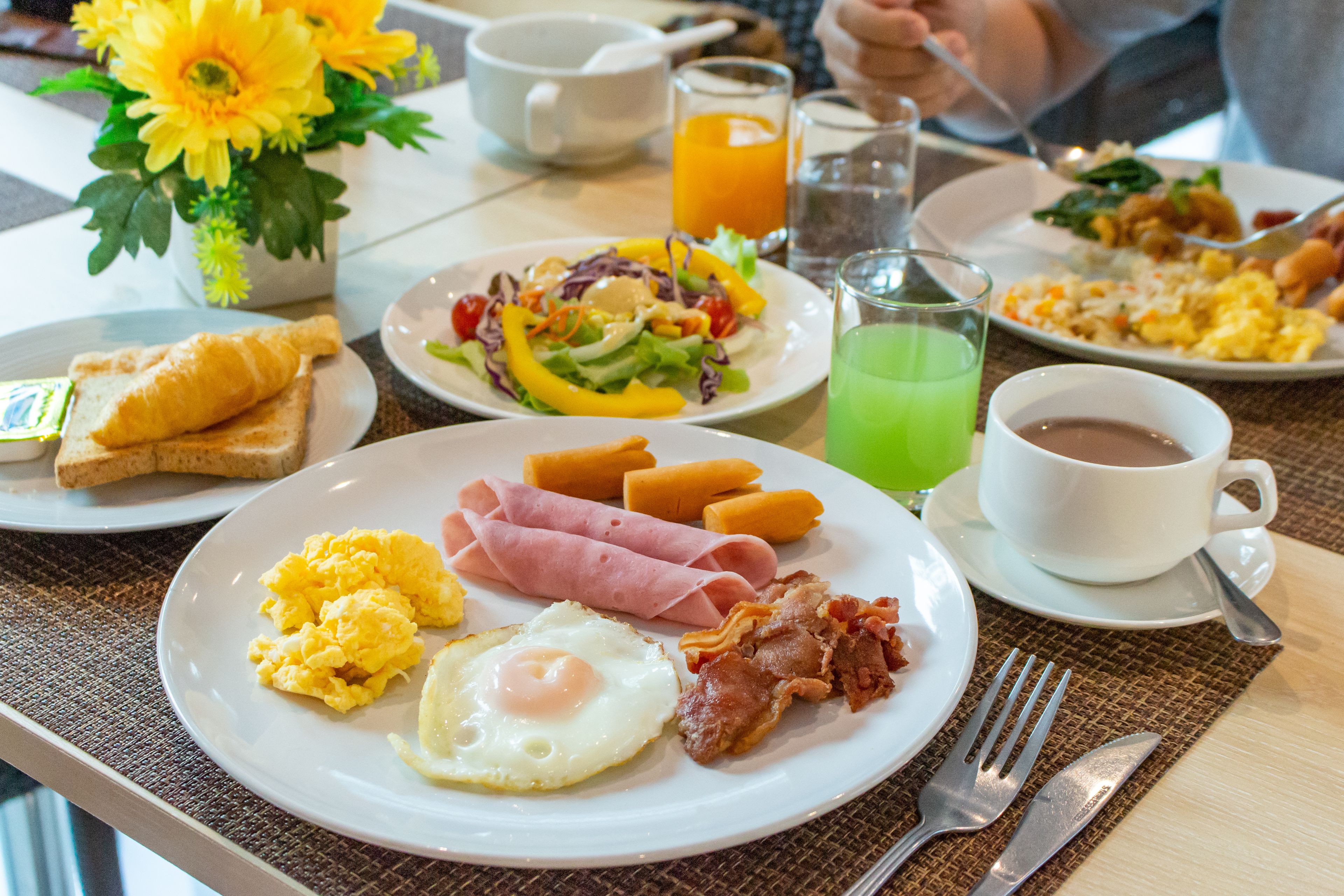 Desayuno con platos de huevos, tocino, jamón, tostadas y una bebida verde.