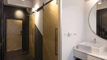 Un baño moderno con puerta de madera, lavabo blanco y espejo.