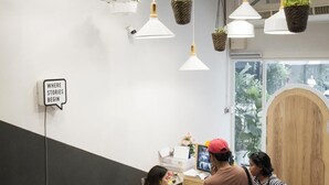 A reception area with a desk, hanging plants, and a sign that reads "WHERE STORIES BEGIN". - Bed One Block Hostel (Bangkok)