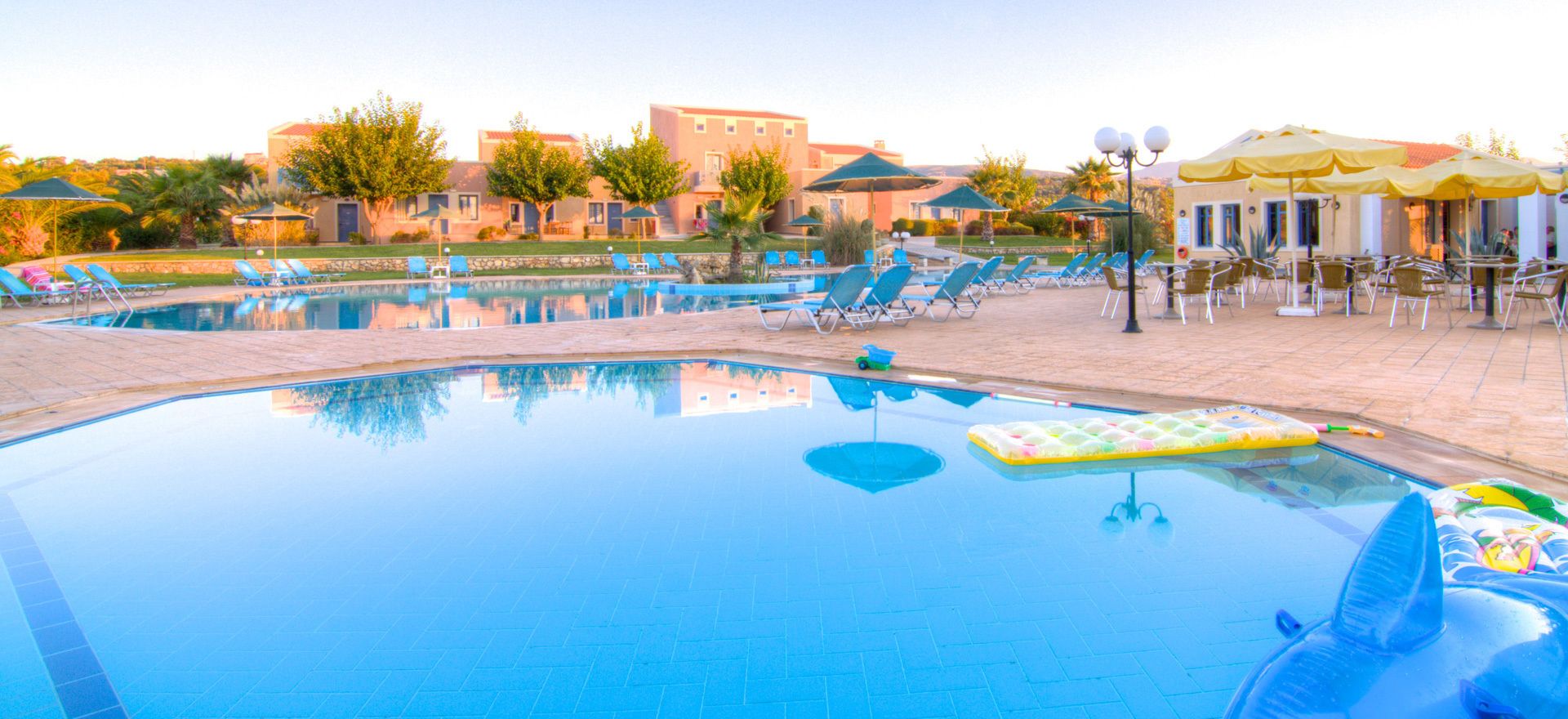 A swimming pool with lounge chairs and umbrellas, surrounded by buildings and trees.