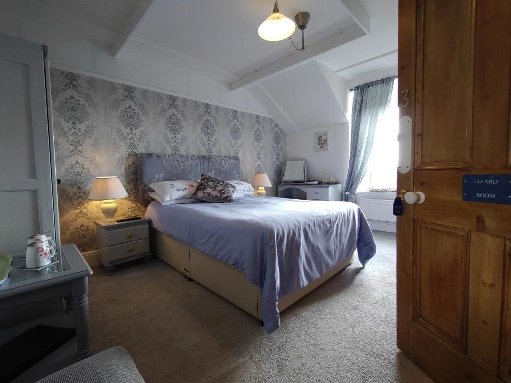 Un dormitorio con cama, lámparas de noche, mesitas de noche, cómoda, una puerta de madera con la leyenda 'LIZARD ROOM' y una ventana con cortinas.