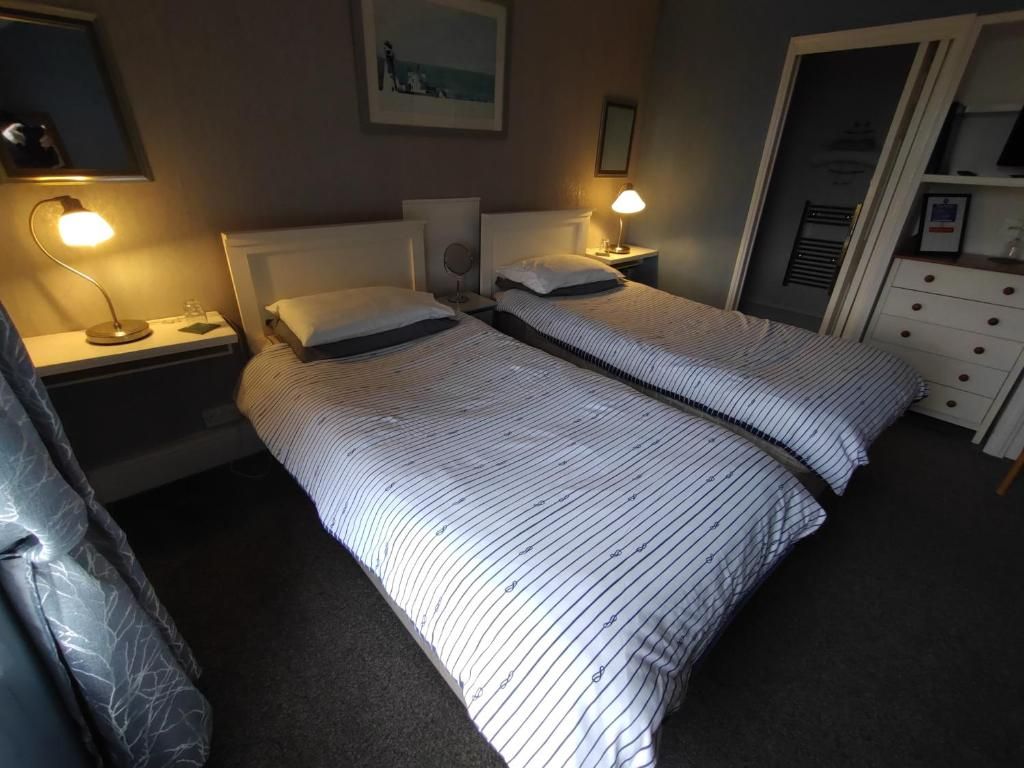 A hotel room with two beds, bedside lamps, a nightstand, a dresser, and a framed picture on the wall.