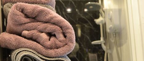 A bathroom with a glass shower door, a towel rack with folded towels, and a white hand dryer.