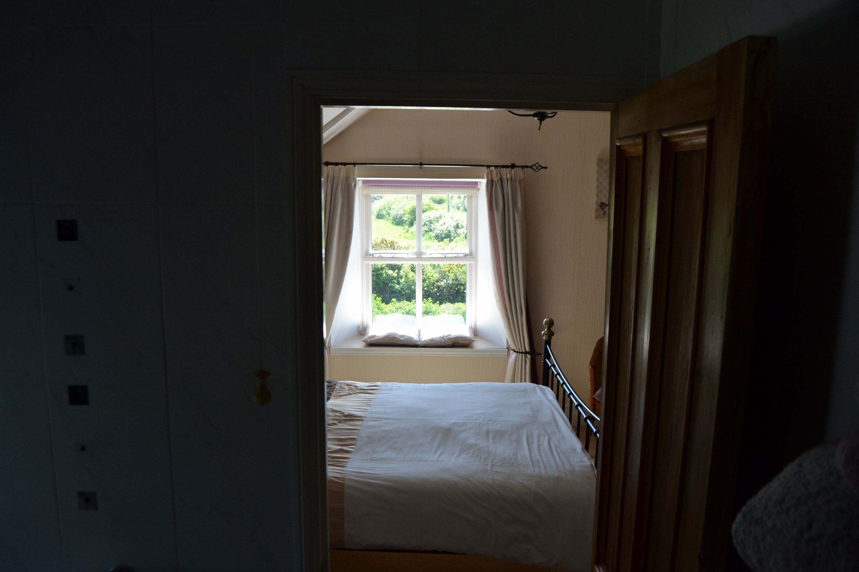 Une chambre avec un lit simple, une fenêtre avec des rideaux et une porte en bois.