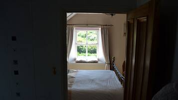 Une chambre avec un lit simple, une fenêtre avec des rideaux et une porte en bois.
