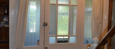 Une porte double blanche avec des panneaux en verre dépoli, un extincteur sur la gauche et un escalier en bois sur la droite.