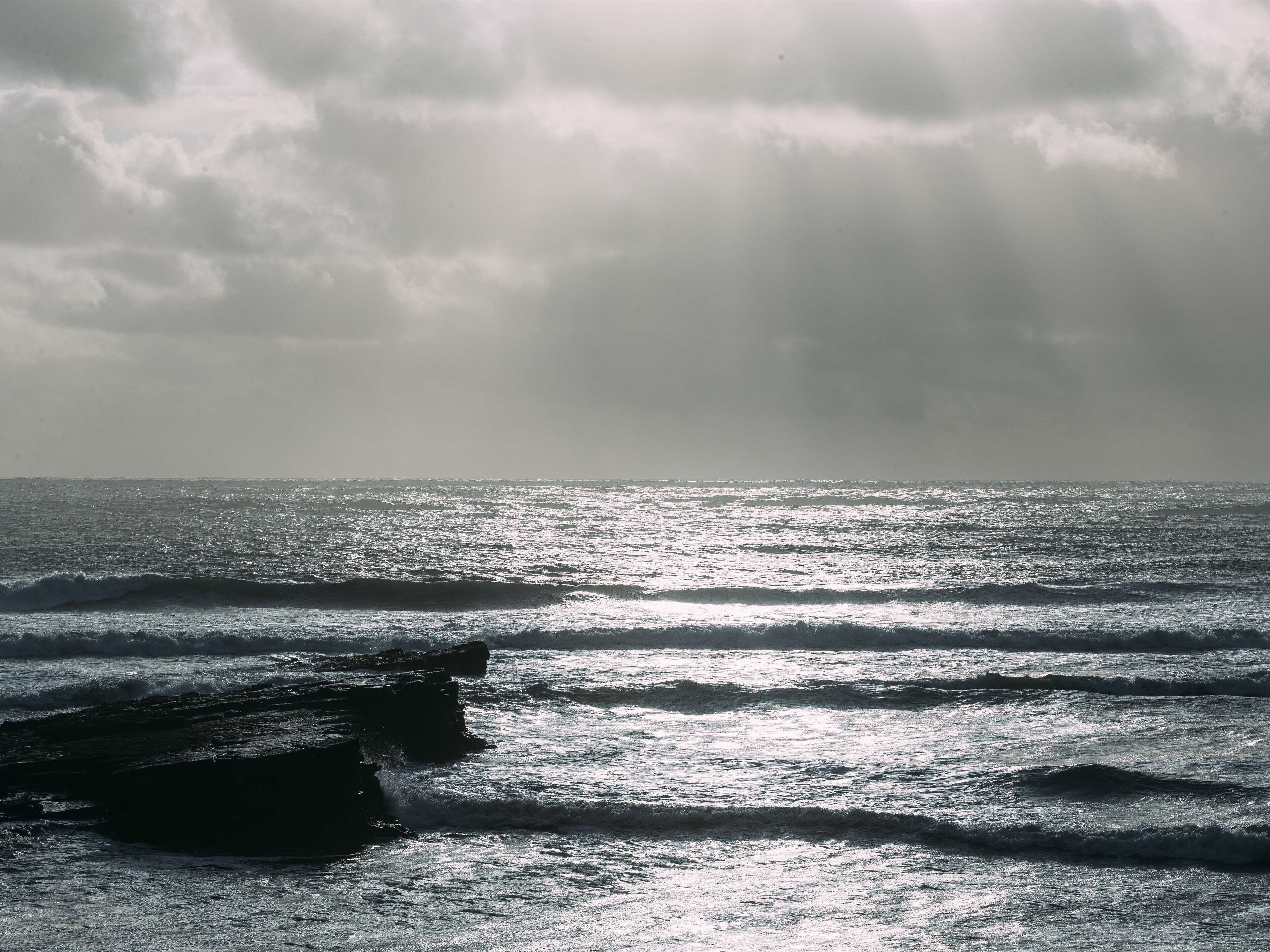 A beach with waves and rocks under a cloudy sky.