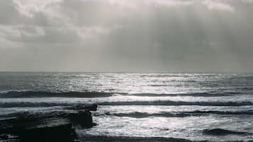 A beach with waves and rocks under a cloudy sky.