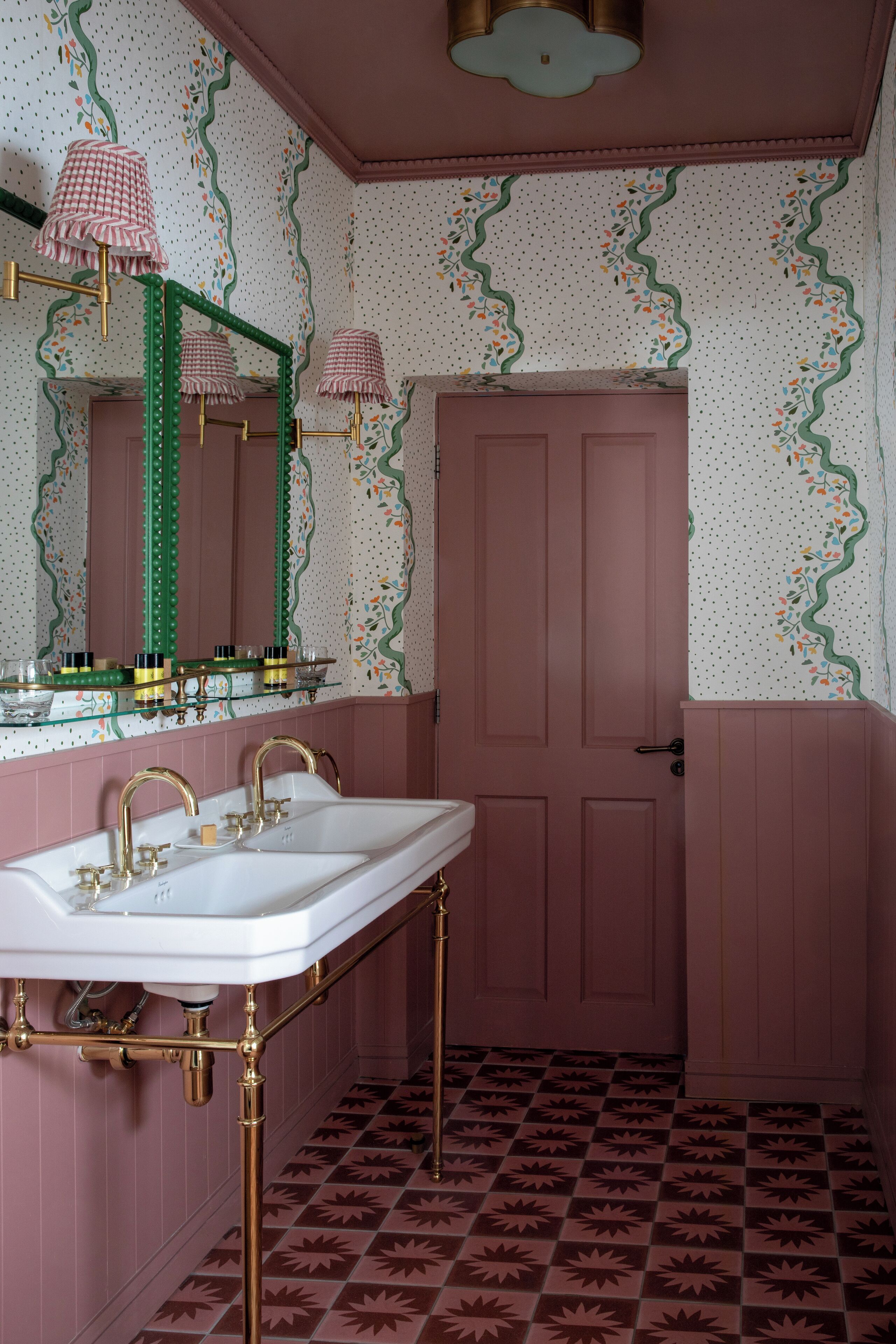 Un baño con una puerta rosa, un lavabo blanco con detalles dorados y un espejo con marco verde.