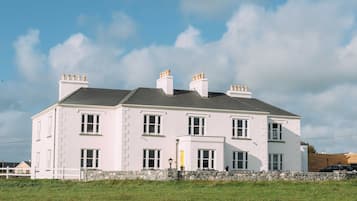 Stunning two-story building with a central entrance and windows on either side, surrounded by a stone wall and lush greenery.