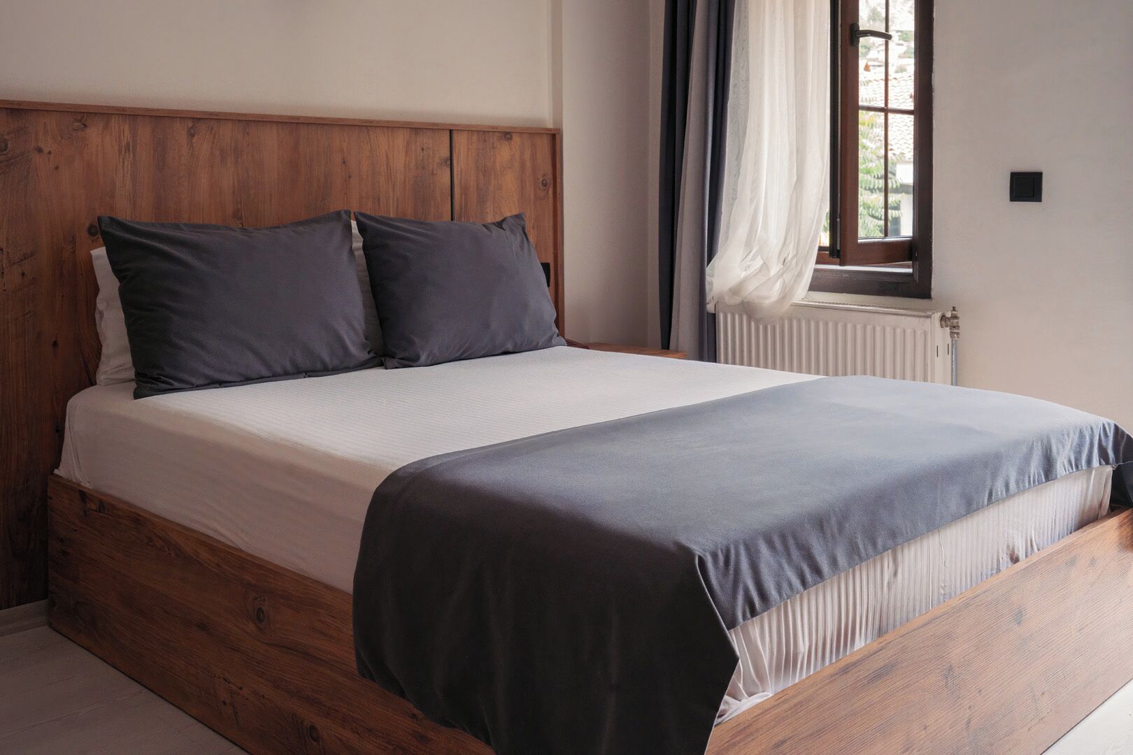 Una cama con estructura de madera y colchón blanco, con dos almohadas oscuras.