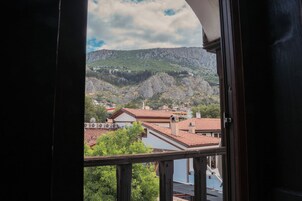 Vista desde una ventana de un edificio con balcón, sobre un pueblo con tejados rojos y montañas al fondo.