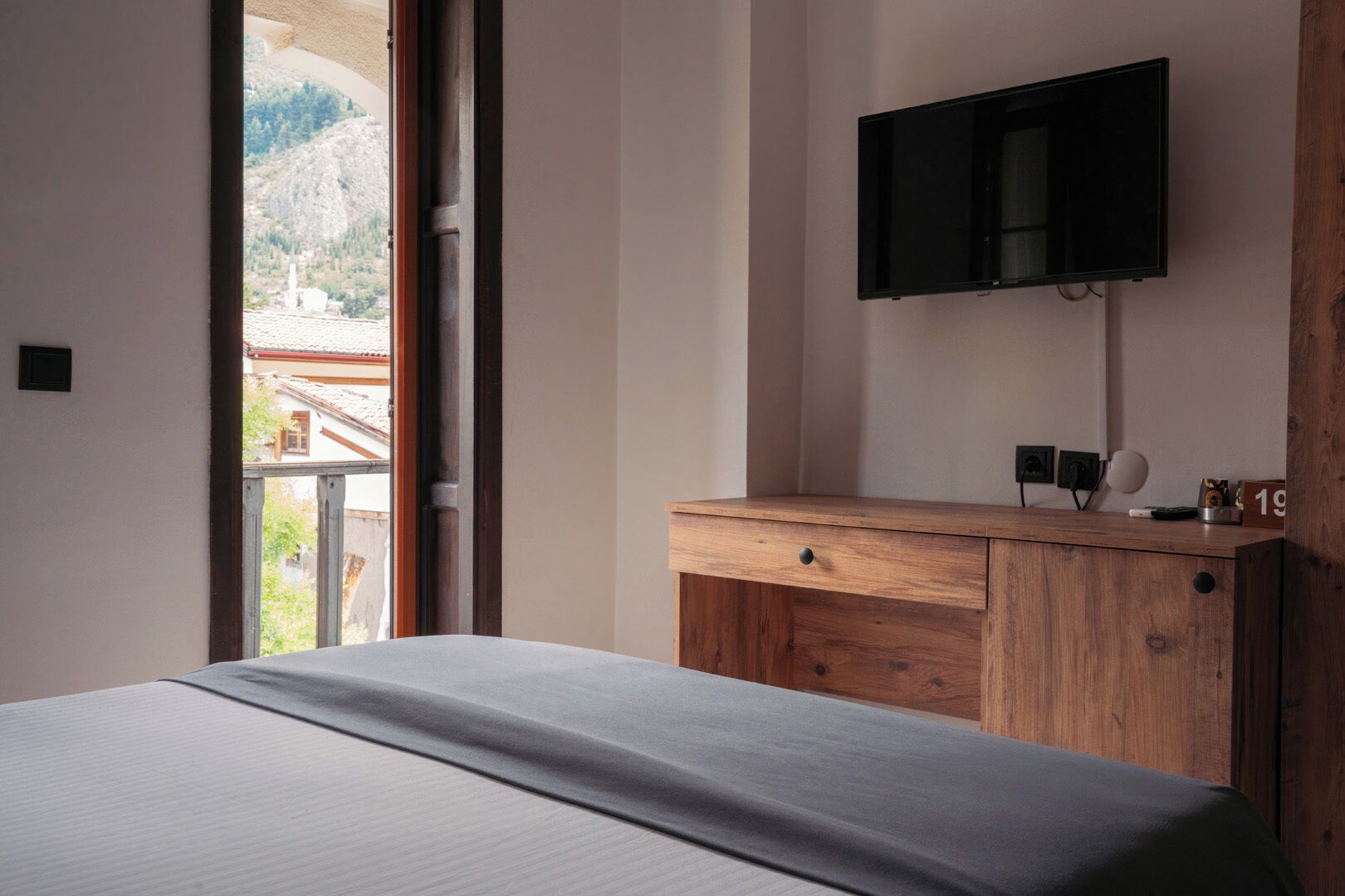 Ein Schlafzimmer mit einem Bett, einer Holzkommode, einem an der Wand befestigten Fernseher und einem Fenster mit Blick auf eine Berglandschaft.