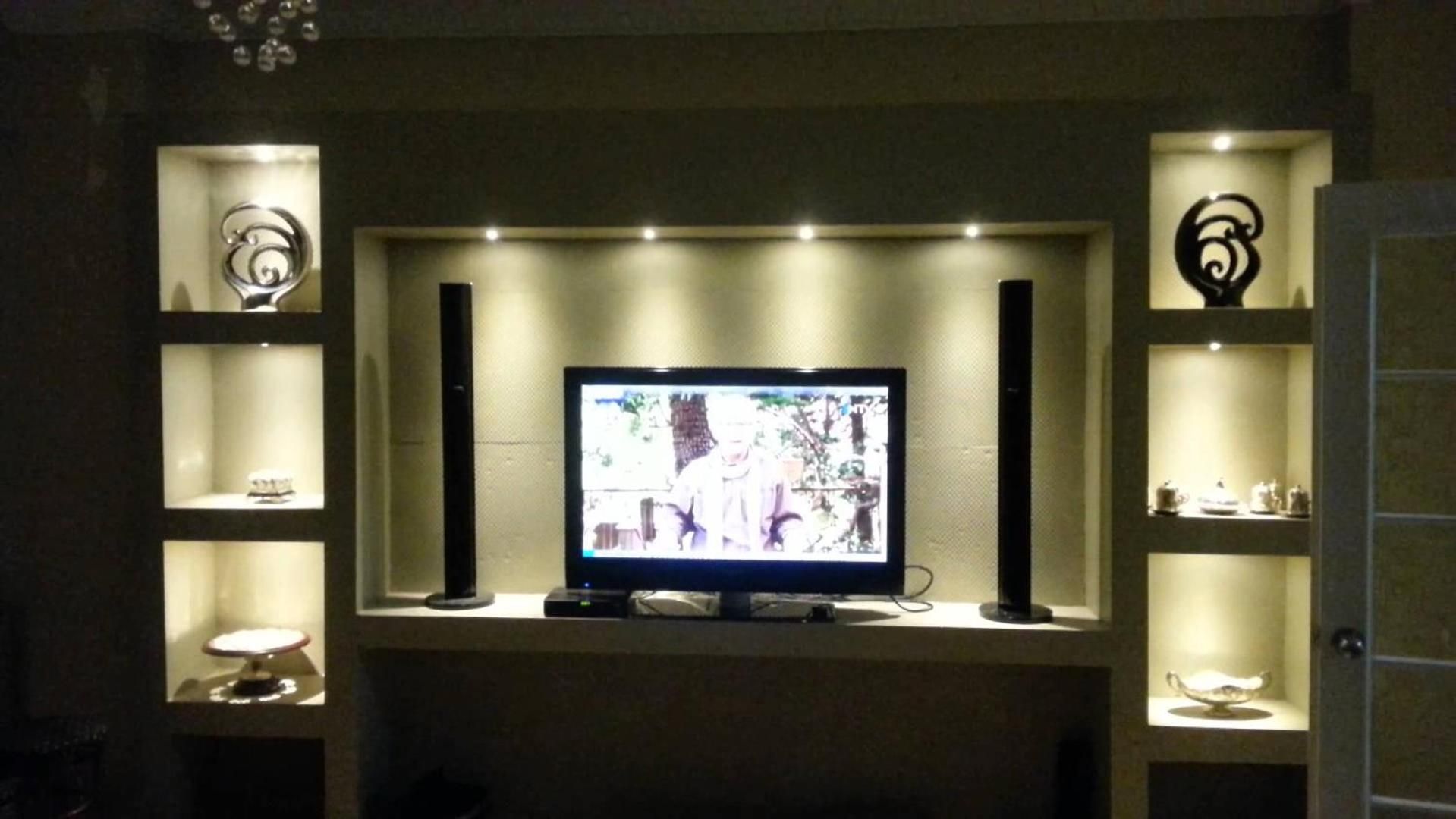 Un téléviseur fixé au mur, avec des étagères de chaque côté.