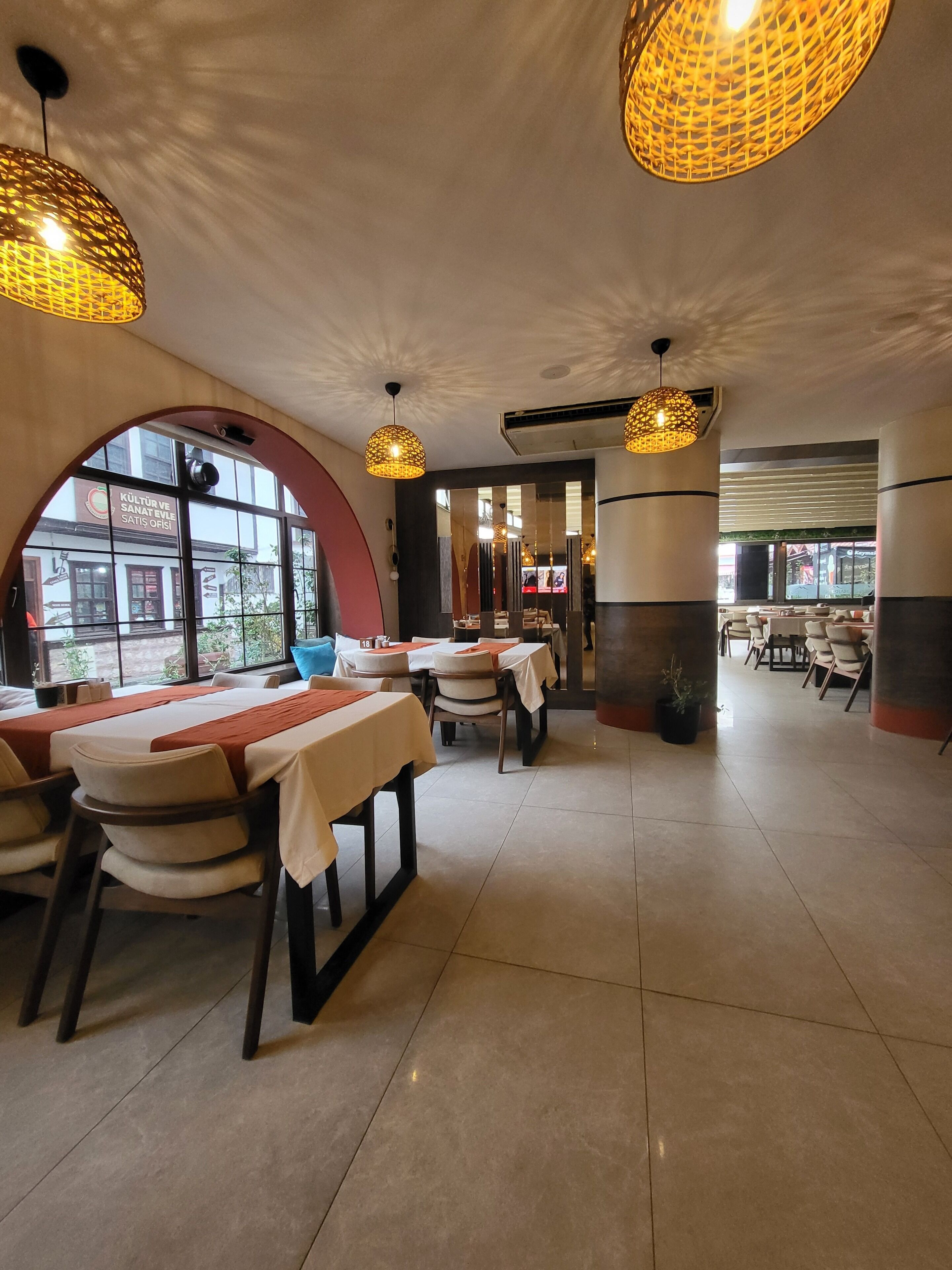 L’intérieur d’un restaurant avec des tables rondes, des chaises et des lampes suspendues.