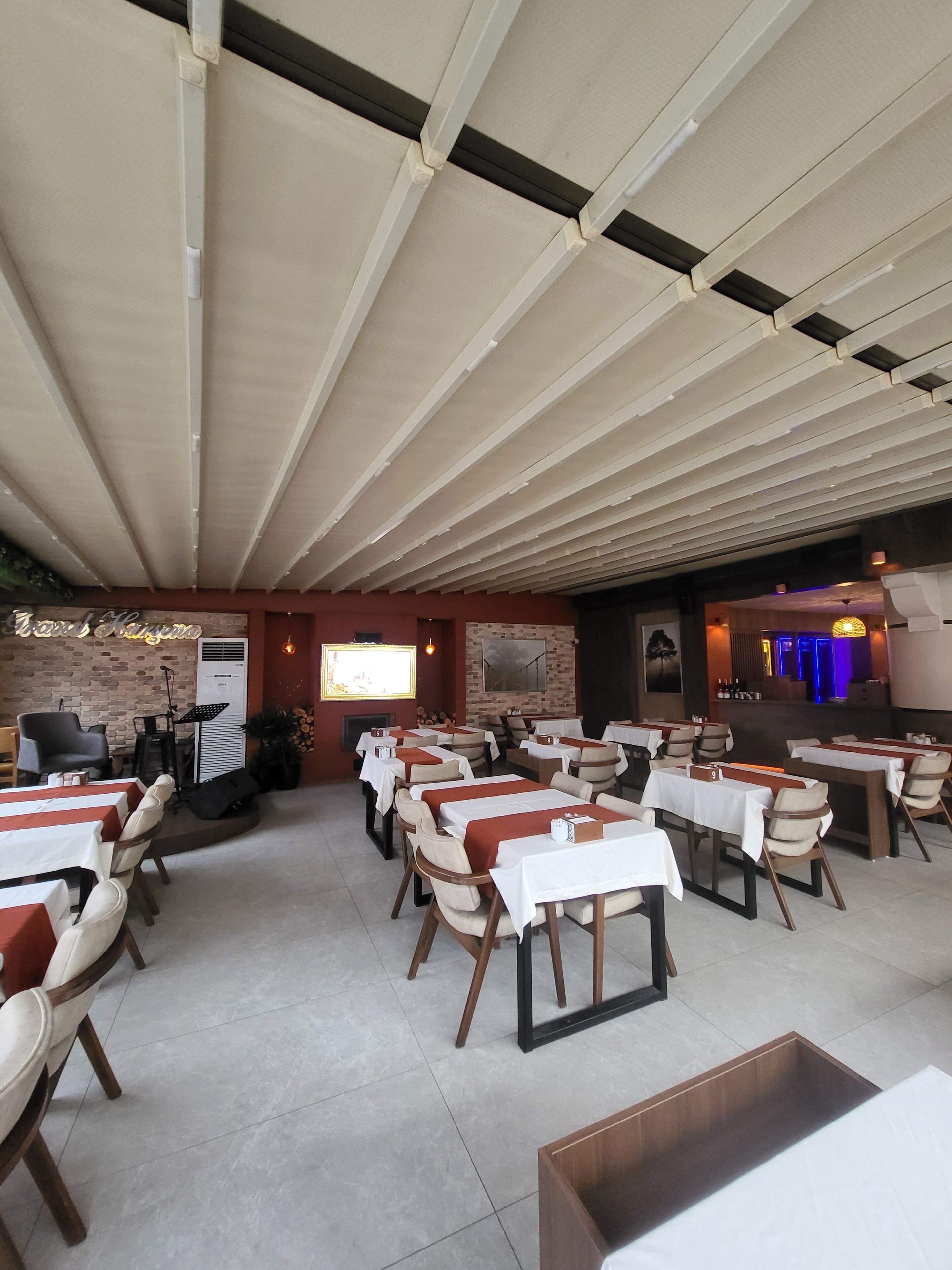 Um restaurante com várias mesas e cadeiras, uma parede de tijolos e um palco com equipamentos musicais.