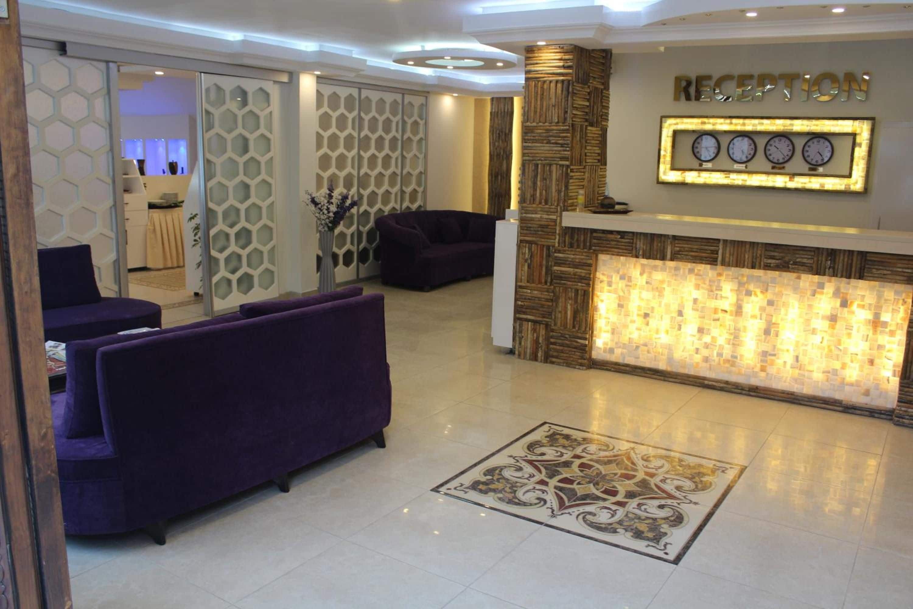 A reception area with a reception desk, two purple sofas, a decorative wall, and a patterned floor.