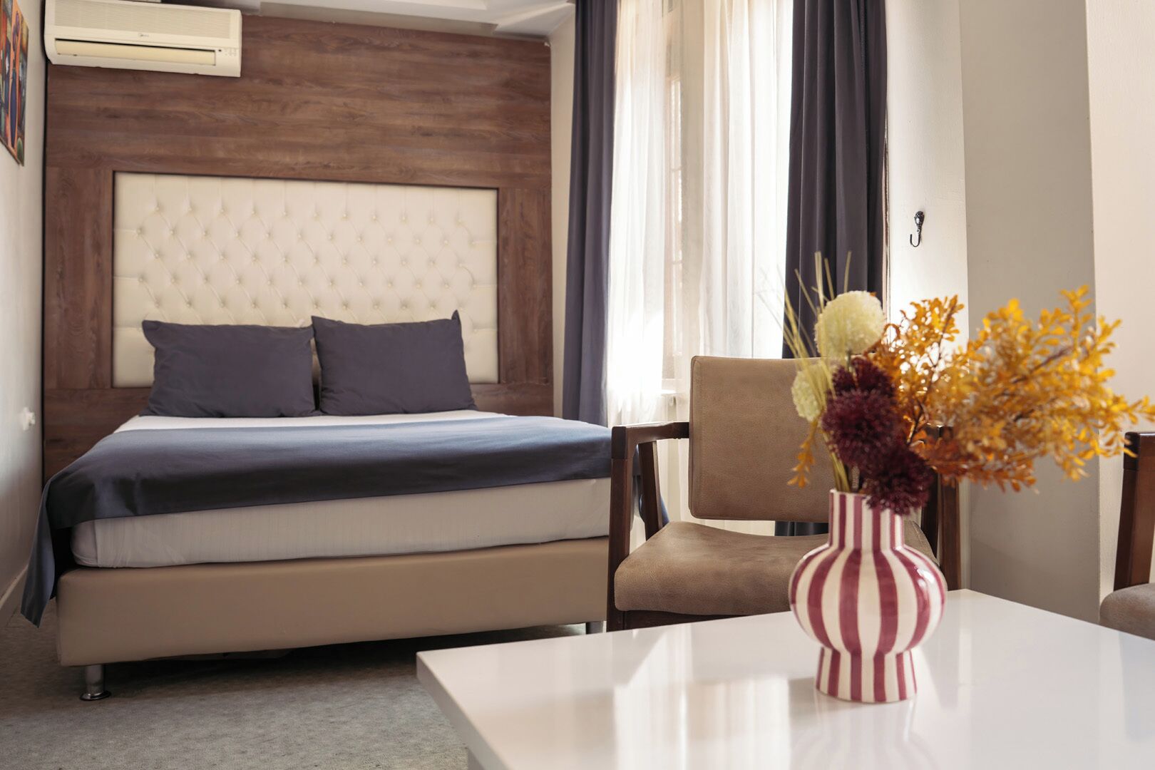 A hotel room with a bed, a chair, a table, and a vase with flowers.