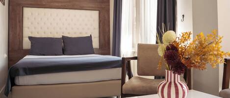 Una habitación de hotel con cama, una silla, una mesa y un florero con flores.