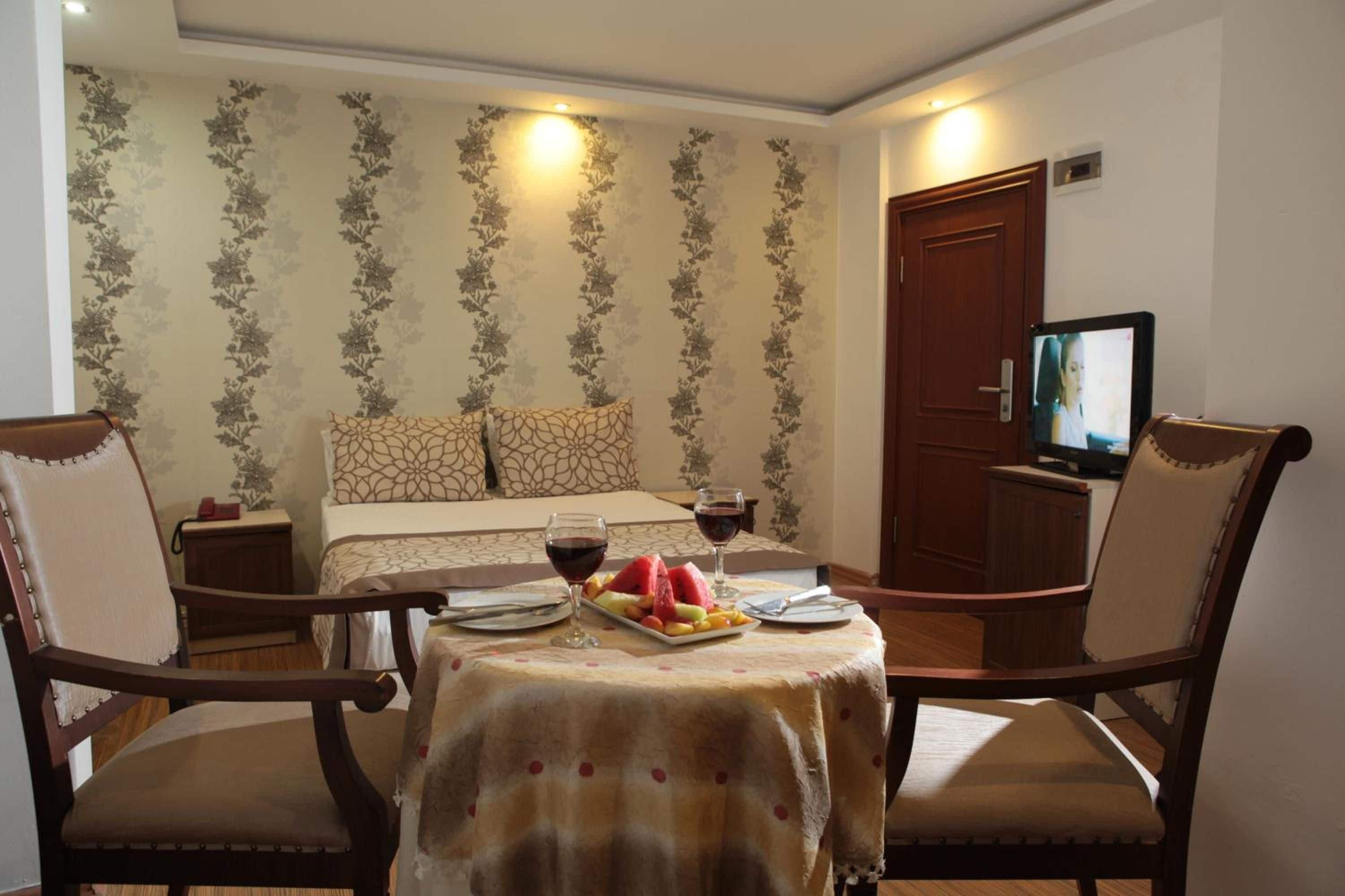 A hotel room with a bed, a television, a dining table with chairs, and a fruit plate.