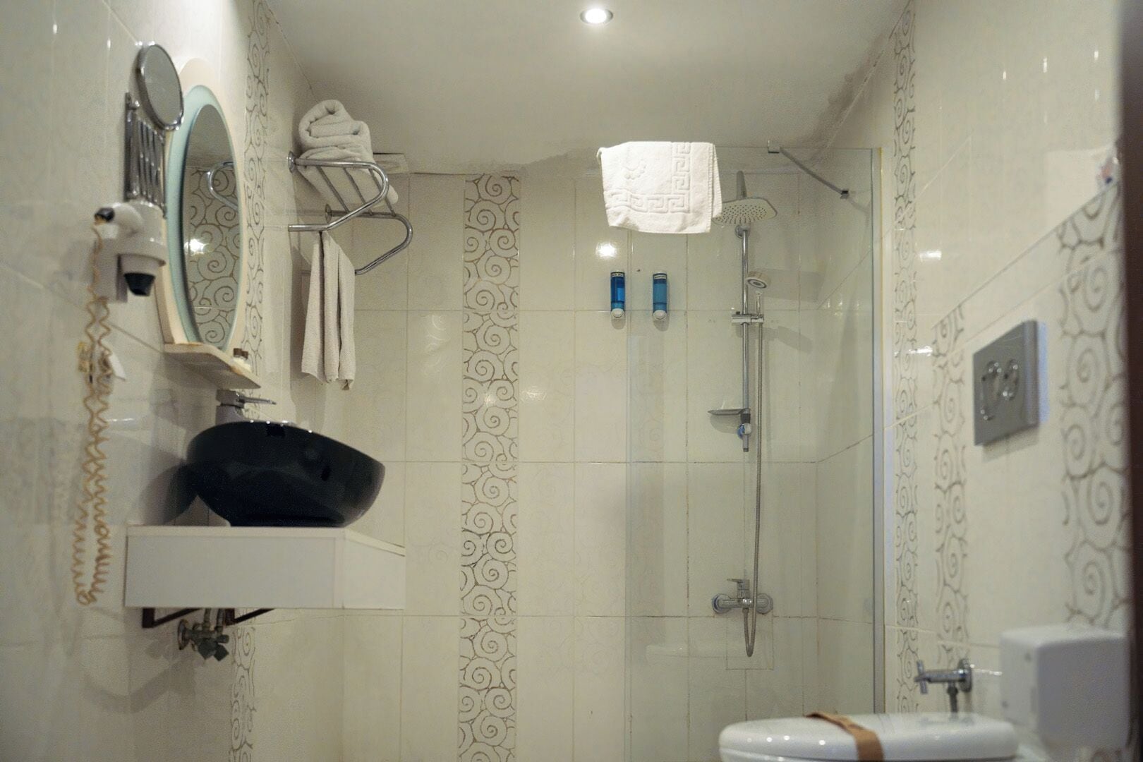 A bathroom with a sink, mirror, towel rack, shower, and toilet.